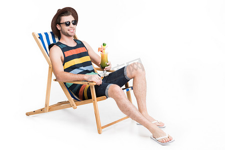 英俊的男子在太阳镜和帽子放松沙滩椅与鸡尾酒, 孤立的白色