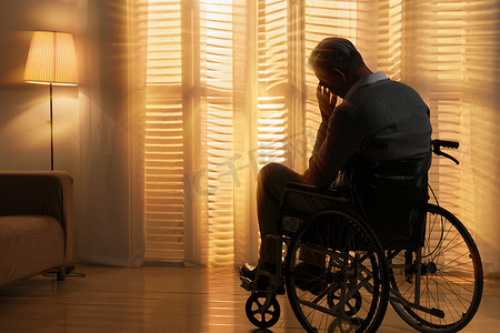 老人烦恼摄影照片_窗前孤独的老年人坐在轮椅上