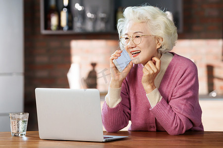 优雅的老年女性边使用电脑边打电话
