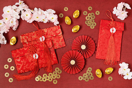 中国新年装饰比红色背景。传统的农历新年红包，纸扇，硬币，金锭，文字意味着财富，繁荣，财富。平躺在地上，俯瞰四周