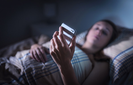 晚上摄影照片_忧心忡忡的女人晚上躺在床上看智能手机。来历不明的电话精神紧张或失眠的不眠者。忧心忡忡或孤独的女士在黑暗的家里用牢房，阅读文字.