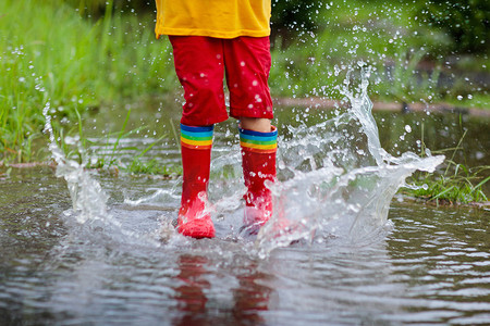 孩子在雨中玩耍。孩子们穿着雨伞和雨靴在外面大雨倾盆地玩耍.小男孩在泥泞的水坑里跳跃.孩子们被秋天的雨天逗乐了.在热带风暴中奔跑的儿童.