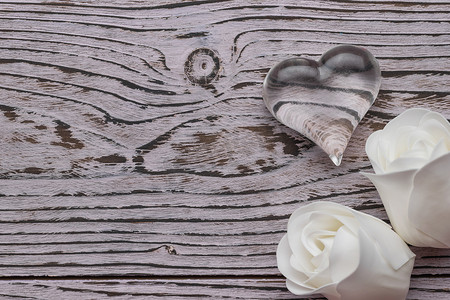 Two white rose buds and a glass heart on a wooden background. The concept of Valentine's Day. Flat lay.