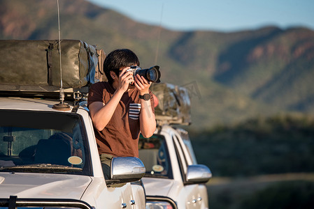 非洲旅游摄影照片_年轻的亚裔男子摄影师在车窗上拍照