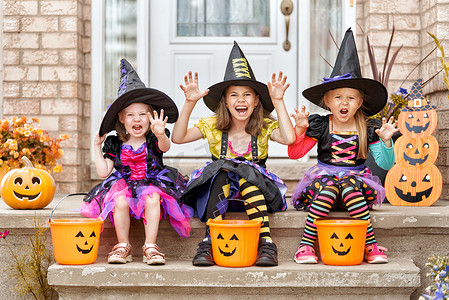 万圣节摄影照片_万圣节快乐！三可爱的小笑的女孩在巫婆服装来的房子糖果.