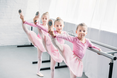 可爱的孩子在粉红色的短裙裙练芭蕾和看在芭蕾学校的相机