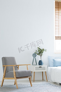 黑色和白色扶手椅站在白色卧室内部与植物和时钟放置在床边的桌子和空墙与地方为您的海报