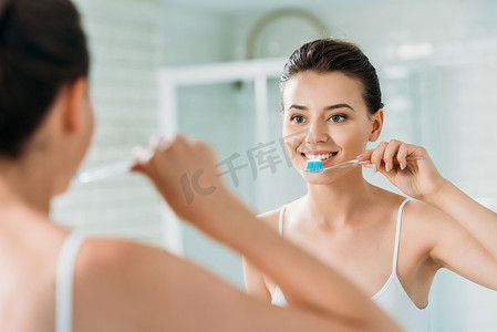 镜子摄影照片_美丽的微笑的女孩刷牙在浴室镜子的牙齿