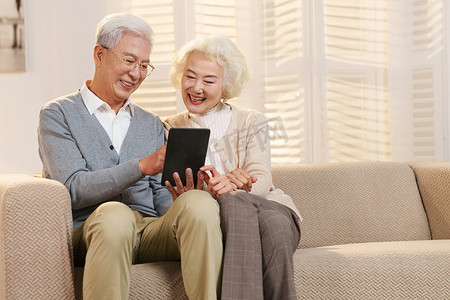 老年沙发摄影照片_老年夫妇坐在沙发上使用平板电脑