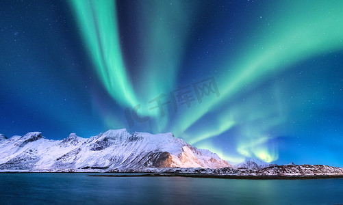 水背景摄影照片_挪威洛福敦群岛上的北极光。山和海岸上方的绿色北极光。夜间冬季景观与极光和反射的水面上。挪威的自然背景