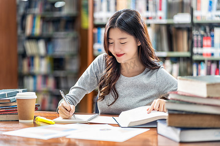 亚洲青年学生穿着休闲服在大学图书馆阅读和做作业，或与各种书籍和固定在书架背景的木桌上，回到学校