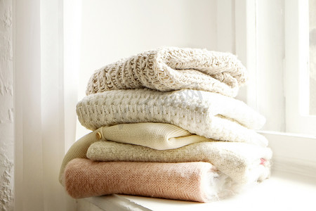 成束的针织保暖胶布色毛衣，不同的针织图案叠叠在白色窗台上，窗台背景。秋天的冬季流行针织衫.关闭，复制空间.