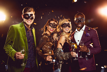 迷人的多民族朋友在狂欢节面具举行香槟杯和庆祝新年派对