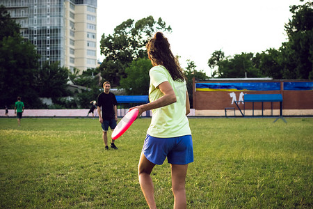 年轻的女人和男人在日落期间玩飞盘在公园里