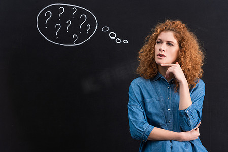 thoughtful redhead young woman with question marks in thought bubble on blackboard