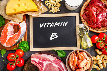 在深色背景下对高维生素B来源进行分类：牛奶、肝脏、橄榄油、西红柿、对虾、花生、牛肉、菠菜、鲑鱼、茄子、茄子、奶酪。顶部视图.