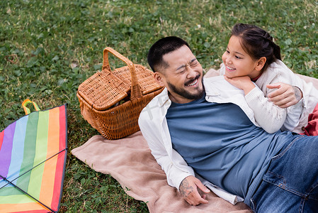 Happy asian dad lying near daughter and wicket basket in park 