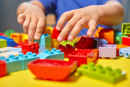 一个漂亮的男孩在家里玩积木游戏。一个可爱的面带微笑的男孩正在和一个房间内有许多彩色塑料块的建筑商玩耍，他正在建造一座城市。学前教育课程.
