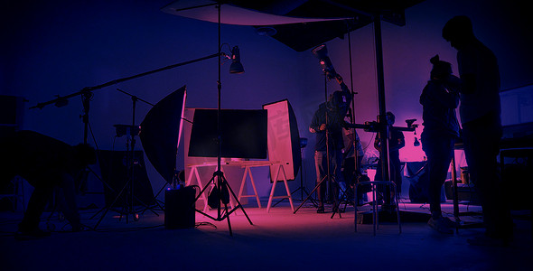 纽蓝粉的色彩拍摄。在大工作室里的视频制作现场后面。摄制组工作和摄像设备在轮廓中.电影制作行业。安装照明装置.