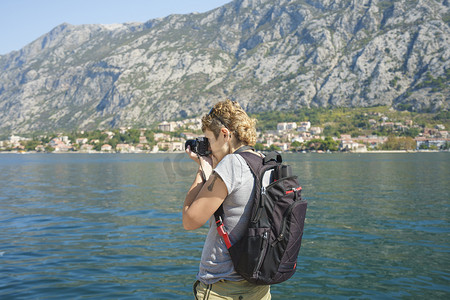 摄影师带着背包照相旅行。女摄影师拍摄与数码单反相机沿着长廊漫步, 在 backgroundgirl 美丽的海洋景观从背后拍摄的海滨长廊