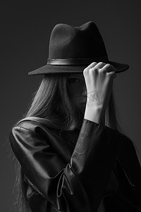 photo摄影照片_monochrome photo of model adjusting fedora hat in studio 