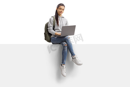 女学生坐在一个有笔记本电脑的空白面板上 