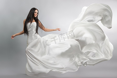 美丽的年轻女孩在飞行白色连衣裙。流动的织物。光白布飞在风中