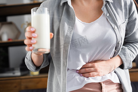 患有乳糖不耐受症的妇女在触摸胃时举着一杯牛奶的剪影 