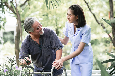 护士与病人使用沃克在退休回家。年轻的女护士手持老人的手在户外花园散步。高级护理、护理人员和高级退休家庭服务概念.