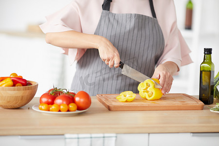 Close-up of woman in apron cutting fresh vegetables with knife on cutting board for salad
