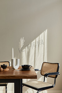 餐厅内部的简约理念，配有木制家庭餐桌、设计椅子、蜡烛棒、咖啡杯、餐具、米色墙壁和个人配饰。复制空间。模板.