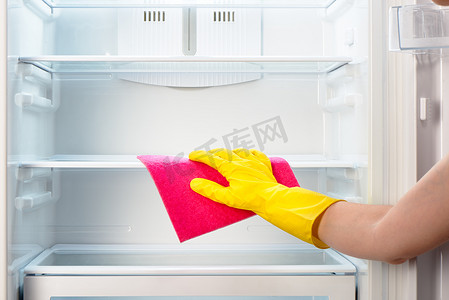 女用手在黄色手套上用粉色抹布擦拭冰箱