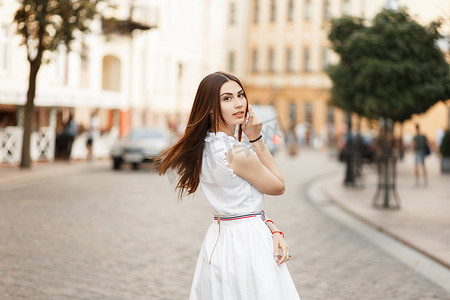 美丽的年轻模特女孩穿着白色时尚的礼服在城市漫步