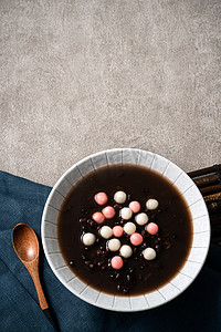 饺子汤圆摄影照片_红白相间的汤圆（汤圆，糯米饺子球）配上甜红豆汤，放在灰色桌旁的碗里，作为冬至佳肴.