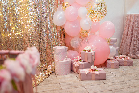 漂亮装饰摄影照片_漂亮的粉色装饰，用缎带和蝴蝶结包裹的礼品盒，金光闪闪的背景上的花朵和气球。婚礼或女孩生日宴会装饰品.