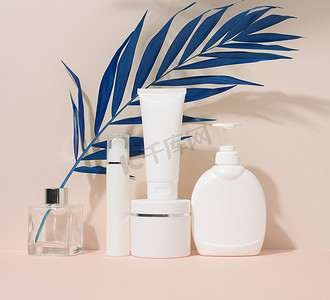 白色塑料容器管，一个有盖的罐子和一个装有药瓶的容器，装有米色背景的化妆品，有棕榈叶的阴影。广告和促销