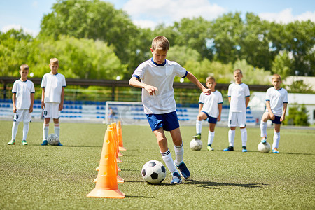 带领摄影照片_少年足球队男童肖像在阳光明媚的日子里在田野练习中带领球