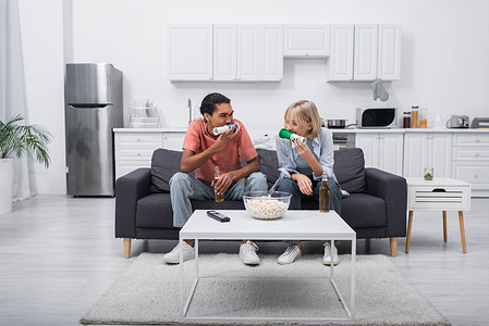 multiethnic couple blowing horns while watching sport match in living room 