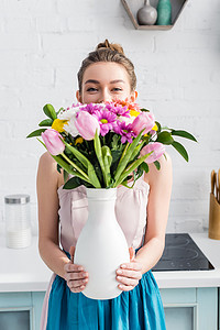 漂亮的女孩与模糊的脸躲在花瓶里的野花花束后面
