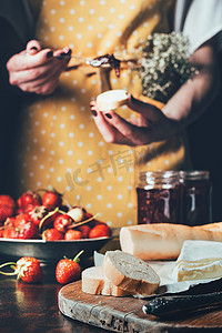修剪的妇女在围裙传播草莓果酱在面包的图片 
