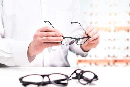 眼镜店里拿着玻璃。眼科医生用镜片。专业验光师在白色外套与许多镜片。商店内部。在眼镜上固定或比较不同的选项.