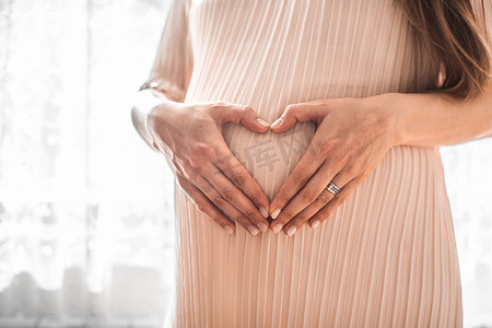 孕妇在婴儿碰撞时双手紧握着心形。带着手指怀孕的美女心形符号。产妇概念。小宝宝洗澡。高恢复图像.