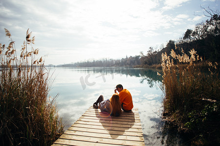 年轻的时髦情侣禧, 爱鸟坐在码头上的公园俯瞰大湖或河在秋季季节。拥抱和拥抱舒适和浪漫, 谈论未来计划和旅行目的地