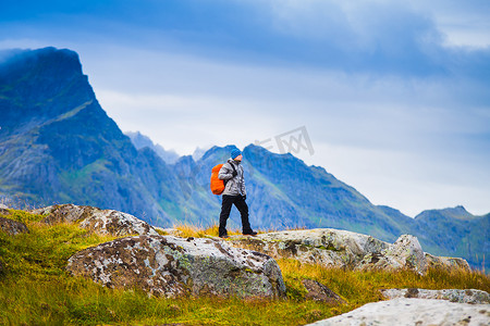 挪威人摄影照片_在挪威徒步旅行。徒步者与红色背包站立在山的背景。人与自然的概念.