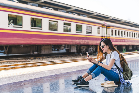限时预定摄影照片_亚洲旅游十几岁的女孩在火车站使用智能手机地图、 社交媒体复选中，或买机票预定。现代旅游应用程序技术，孤独的旅行者，夏天假期铁路冒险概念
