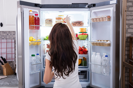 一个年轻女子从冰箱里吃东西的后视镜