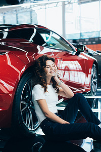 快乐的女人有选择的焦点, 闭着眼睛坐在新的红色汽车附近的地板上