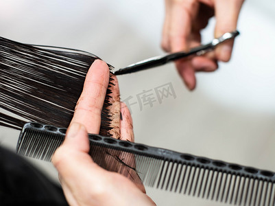 头发护理的主题。一个女理发师在美容院里给顾客剪头发。理发师用梳子、剪刀和头发的手显示了特写. 