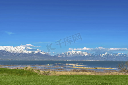 雪山湖面摄影照片_阳光明媚的蓝天下，有湖面和雪山景色的草地
