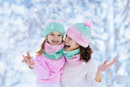 在家庭圣诞假期，戴着针织冬季帽子的母亲和孩子们在雪地里玩耍。给妈妈和孩子的手工羊毛帽子和围巾.给孩子们织毛衣针织外套。雪地公园里的妇女和小女孩.